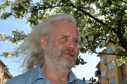 Fredrik Ahlkvist har gråvitt skägg och dito långt hår. idyllisk sommarbild med mycket grönska.